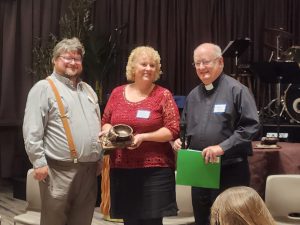 Three people at an indoor event, one holding a trophy.