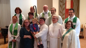 A group of twelve people, many in religious robes, pose together. One person holds a child in a blue shirt and red tie.