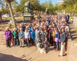 A large group of people pose for a photo in front of a statue and trees.