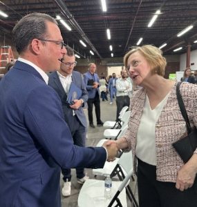 Two people shaking hands in a large indoor space with chairs and people in the background.