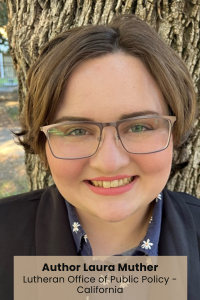 Person smiling in front of a tree, wearing glasses and a dark blazer.