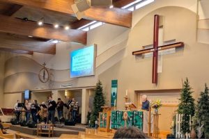 Interior of a church with a cross, lectern, musicians, and projected text.