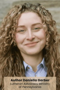 A person with long, curly hair wearing a blue, collared shirt, stands against a blurred background.