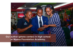 The image features three individuals indoors, under bright lighting. In the center, a person wearing a blue school uniform, including a blazer and tie, holds a phone. On the left, another person in a black polo shirt with a visible logo is engaged in conversation. On the right, a third person is wearing a striped dress and glasses, attentively looking at the phone. Behind them, a group of people is seated, and colorful, decorative elements adorn the room's walls. Transcribed Text: Our author (photo center) in high school at Mpesa Foundation Academy.