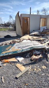 A damaged sign on the ground in front of a destroyed building.