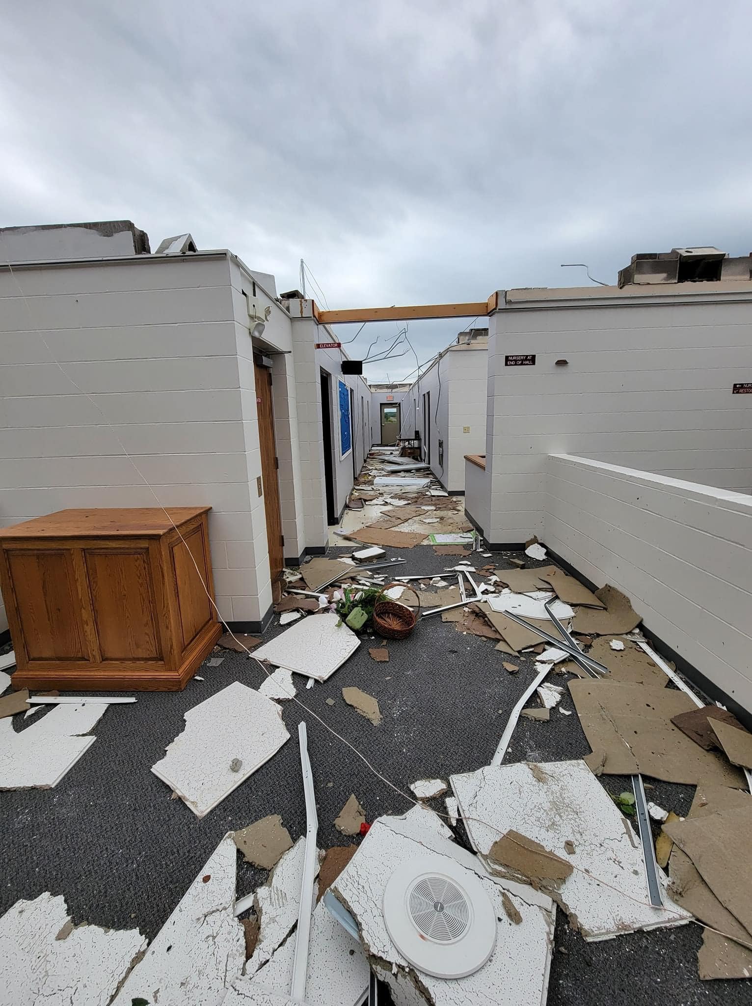 A long hallway scattered with debris and missing the roof.